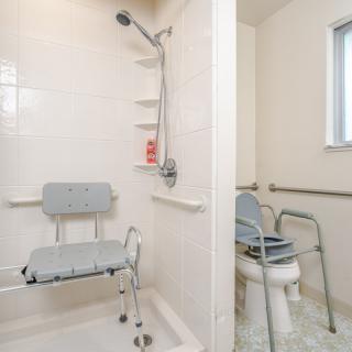 An accessible bathroom featuring a shower with a shower chair and grab bars, alongside a toilet with support rails.
