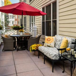A cozy patio setup with comfortable seating, vibrant cushions, a large umbrella, and decorative flowers.