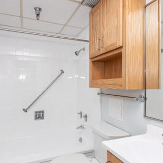 A clean bathroom featuring a shower with a grab bar and wooden cabinets.