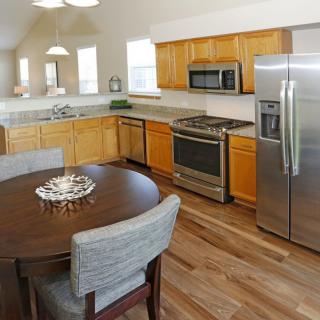 A modern kitchen with wooden cabinets, stainless steel appliances, and a dining area.