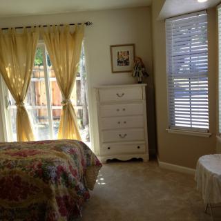 A cozy bedroom with natural light streaming in through the windows and yellow curtains framing a view of the garden.