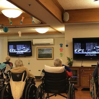 Elderly residents in a nursing home gather to watch television together.