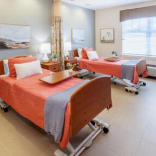 A well-lit hospital room with two neatly made beds and bedside tables.