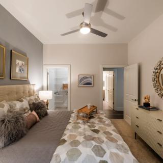 A cozy bedroom with neutral tones, featuring a ceiling fan, artwork, and a neatly arranged dresser.