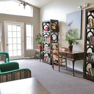 A cozy living room with bookshelves, a desk, and bright natural lighting.