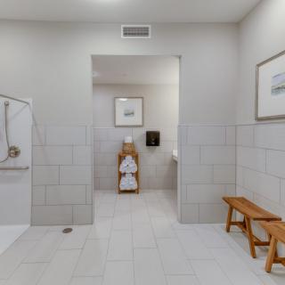 A spacious bathroom with a walk-in shower, neatly folded towels on a wooden rack, and a bench for seating.