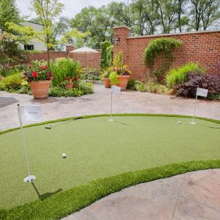 A backyard featuring a well-maintained putting green surrounded by lush garden landscaping.
