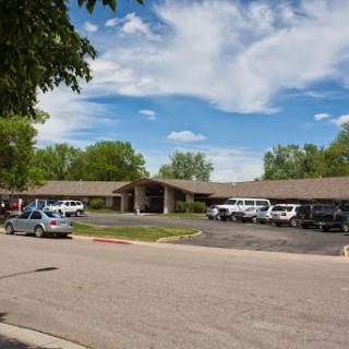 A sunny day view of a building surrounded by vehicles in the parking lot.