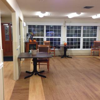 An empty room with tables and chairs, featuring large windows and wooden flooring.