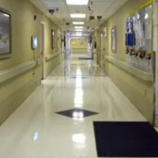 A clean, well-lit hospital hallway with tiled flooring and decorations on the walls.
