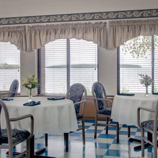 A cozy dining room with neatly arranged tables and chairs, featuring large windows with curtains.