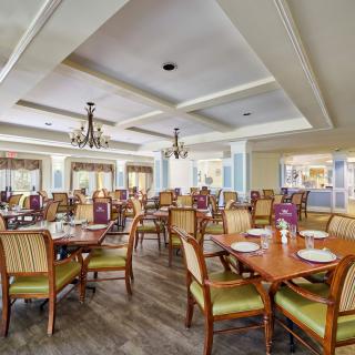 A spacious and elegantly designed restaurant dining area with wooden tables, comfortable chairs, and ornate chandeliers.