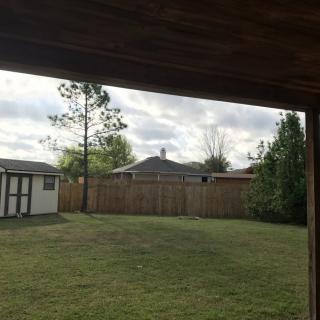 A view of a backyard with a lawn, wooden fence, shed, and trees under a cloudy sky.