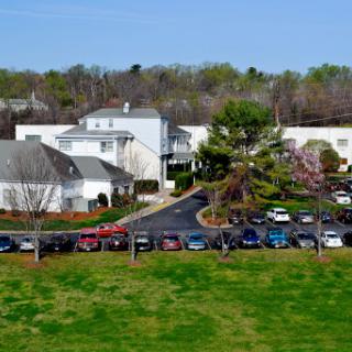 Aerial view of a residential area featuring buildings, a parking lot filled with cars, and green grass.