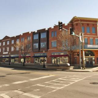 A street view of a brick building with multiple storefronts at an intersection.