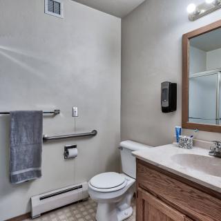 A clean and modern bathroom with a toilet, sink, mirror, and handrail.