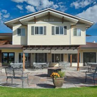 A modern two-story house with a spacious patio, featuring outdoor seating and surrounded by a well-maintained lawn under a blue sky with clouds.