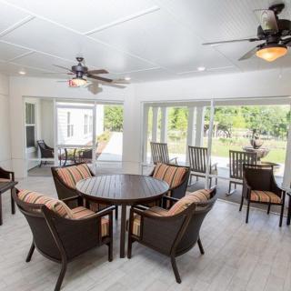 A spacious, bright interior patio with round tables and chairs, surrounded by large windows overlooking greenery.