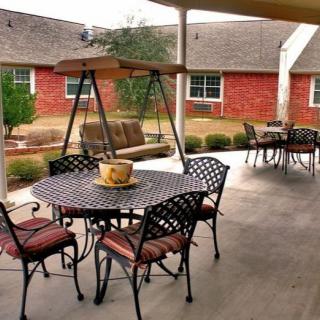 A cozy outdoor patio featuring a swing, tables, and chairs under a covered area.