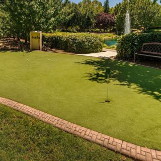 A serene garden featuring a putting green, surrounded by lush trees and a bench for relaxation.