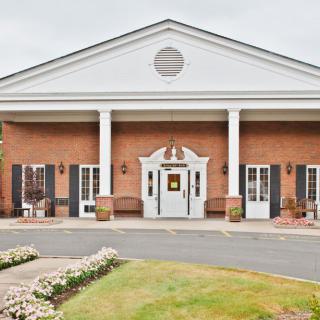 A brick building with white columns and a well-maintained landscape at the entrance.