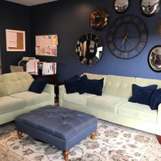 A stylish living room with light-colored couches, navy pillows, a large wall clock, and decorative mirrors.