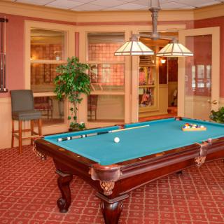 A cozy billiards room featuring a pool table with green felt, classic wood furniture, and warm lighting.