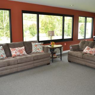 A spacious living room featuring two gray sofas, large windows with abundant natural light, and a cozy carpeted floor.