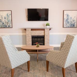 A cozy living room setup with patterned chairs and a television above the fireplace.