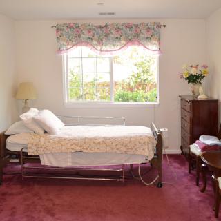 A simple bedroom with a hospital bed, decorated with floral curtains and a burgundy carpet.