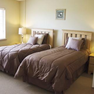 A cozy bedroom with two twin beds, each adorned with brown comforters and pillows, softly lit by a lamp on a wooden nightstand.