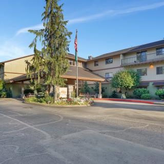 The exterior of a hotel building with an entrance surrounded by trees and a clear sky.