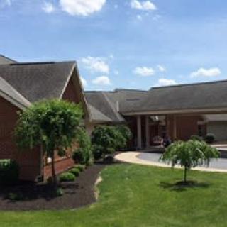 A suburban brick house with a well-maintained lawn and landscaping under a clear blue sky.