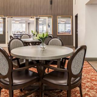 A cozy dining area featuring a round table surrounded by chairs, adorned with a vase of flowers on a patterned carpet.