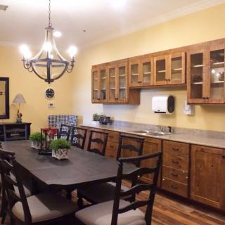 A cozy dining area with a wooden table and chairs, illuminated by a chandelier, adjacent to a kitchen space with wooden cabinets.
