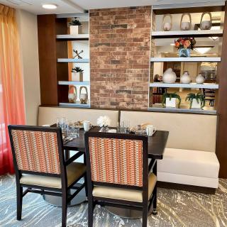 A modern dining area with elegant seating and decorative shelving, featuring a brick accent wall.