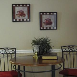 A cozy dining nook with a round wooden table, two chairs, wall art, and a potted plant.