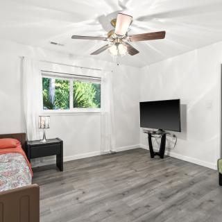 A modern, minimalist bedroom with a bed, TV, and ceiling fan.