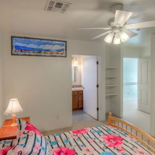 A cozy bedroom featuring a ceiling fan, colorful bedding, and an adjoining bathroom.