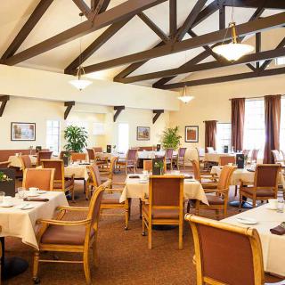 A spacious dining area with neatly arranged tables and chairs, featuring rustic ceiling beams and potted plants for decor.