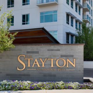 A modern building with a prominent sign for 'The Stayton' surrounded by landscaped greenery.