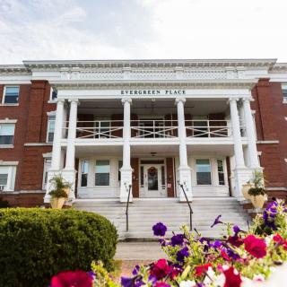 A historic building with a grand entrance featuring white columns and vibrant flowers in the foreground.