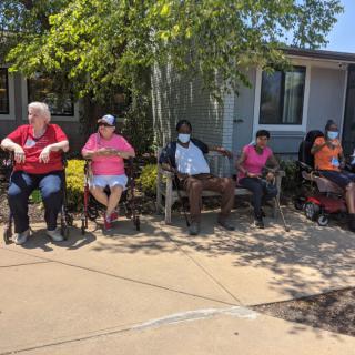 A group of people sitting on benches outdoors on a sunny day.
