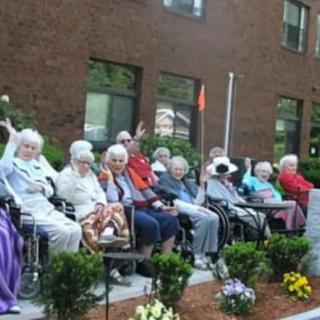 A group of elderly individuals sitting in wheelchairs outside a building, enjoying the outdoors.