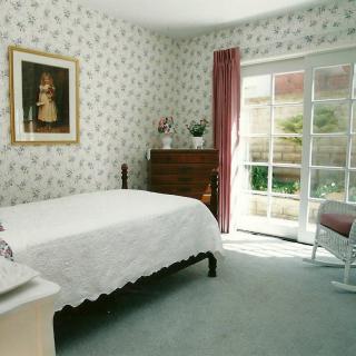 A cozy bedroom with floral wallpaper, a large bed, and sunlight streaming through glass doors.