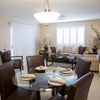A modern dining and living area featuring a glass dining table set elegantly with dishware, surrounded by cozy seating and contemporary furnishings.