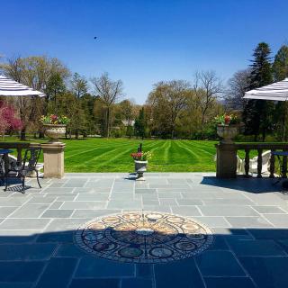 A sunny view of a patio overlooking a well-manicured lawn and garden.