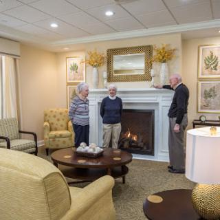 A cozy living room where two seniors engage in conversation while standing near a fireplace.