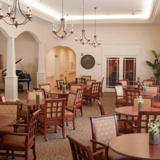 A spacious and elegant dining area with wooden tables and chairs, adorned with chandeliers and a piano in the corner.