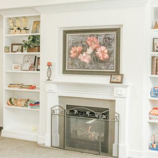 A cozy living room featuring a fireplace with decorative shelves, adorned with artwork and books.